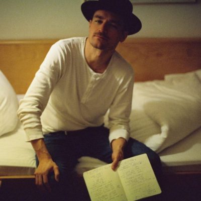 Musiker Christian Schüll sitzt auf einem Bett mit einem Textbuch